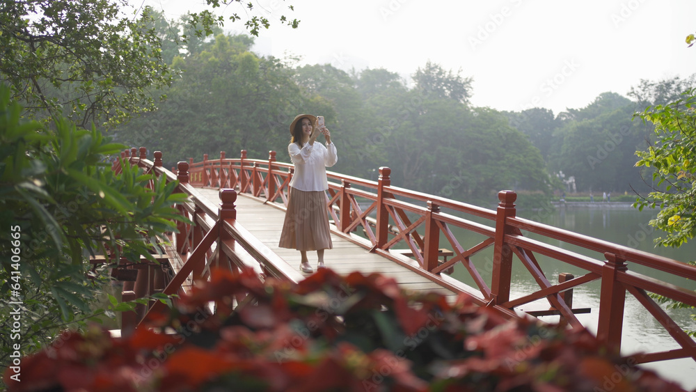 Portrait of Asian Vietnamese woman travel in The Red Bridge in public park garden with trees in Hoan Kiem Lake in Downtown Hanoi. Urban city, Vietnam.. Portrait of Asian Vietnamese woman travel in The Red Bridge in public park garden with trees in Hoan Kiem Lake in Downtown Hanoi. Urban city, Vietnam..