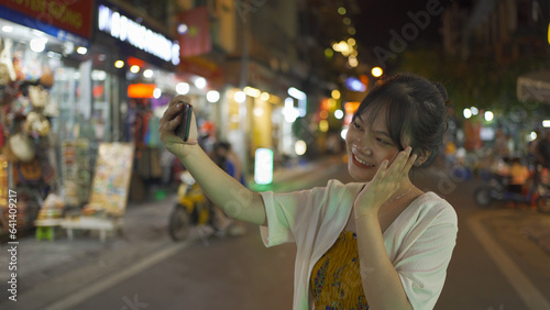 Cuadro en lienzo Portrait of happy Asian Vietnamese woman travel at night market, using mobile phone in technology device in people walking street fair in Hanoi city, Vietnam