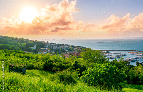 panoramic landscape view of green summer city with yellow houses  green forest and mountains above and amazing hills and cloudy sky on background