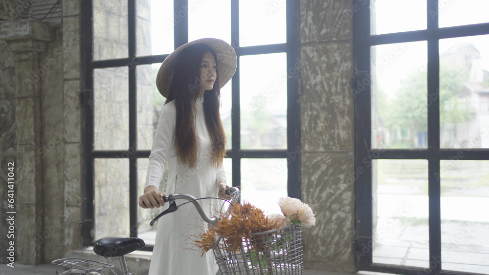Portrait of Asian Vietnamese woman with Vietnam dress and straw hat riding a bicycle or bike in Hanoi. People lifestyle.