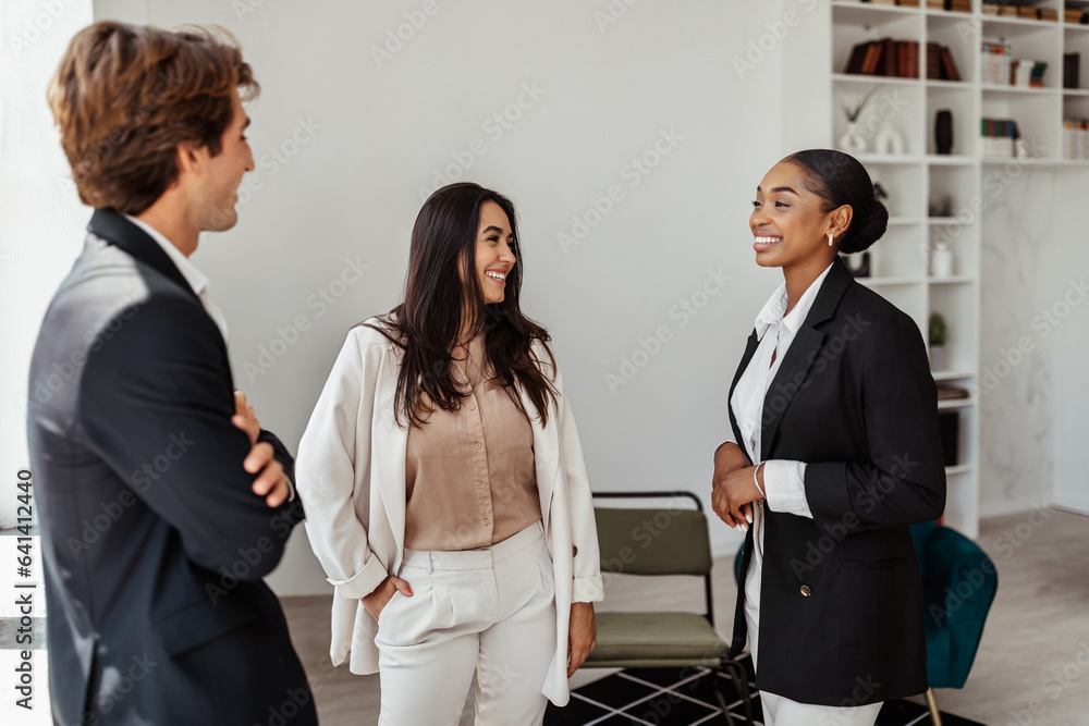 Friendly multiracial young colleagues office workers standing in conference room and chatting at break Friendly multiracial young colleagues office workers standing in conference room and chatting at break