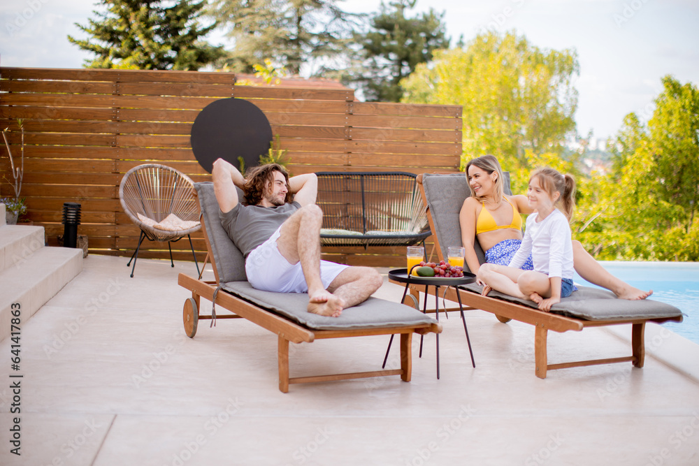 Obraz na plátně Family with a mother, father and daughter sitting on the deck chairs by the swim
