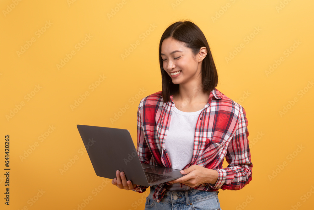 Remote work and education. Happy young asian woman holding laptop for surfing in internet, yellow studio background Remote work and education. Happy young asian woman holding laptop for surfing in internet, yellow studio background