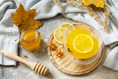 Hot herbal vitamin sea buckthorn tea in a glass cup with fresh sea buckthorn berries  honey and lemon on a stone tabletop. Relaxation and herbal medicine.