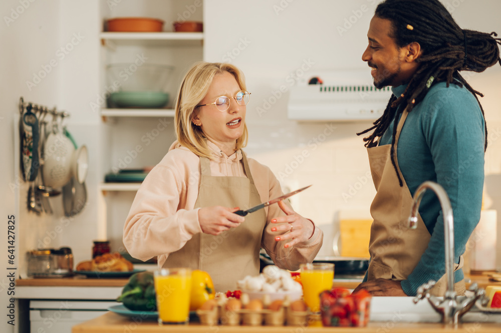An interracial couple is cooking a meal while talking in the kitchen. An interracial couple is cooking a meal while talking in the kitchen.