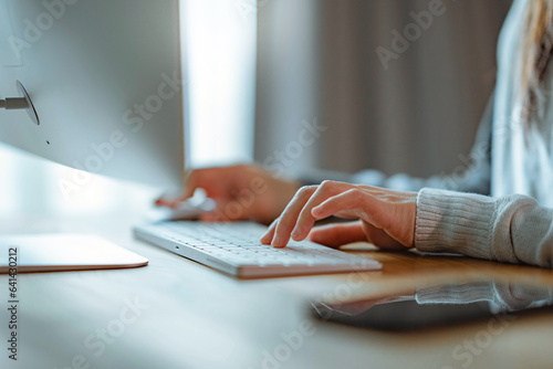 Closeup hand of a woman working and typing on keyboard computer on wooden table at home.