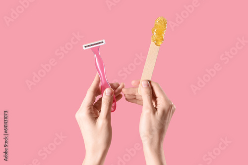 Hands holding spatula with sugaring paste and razor on pink background. Hair removal concept