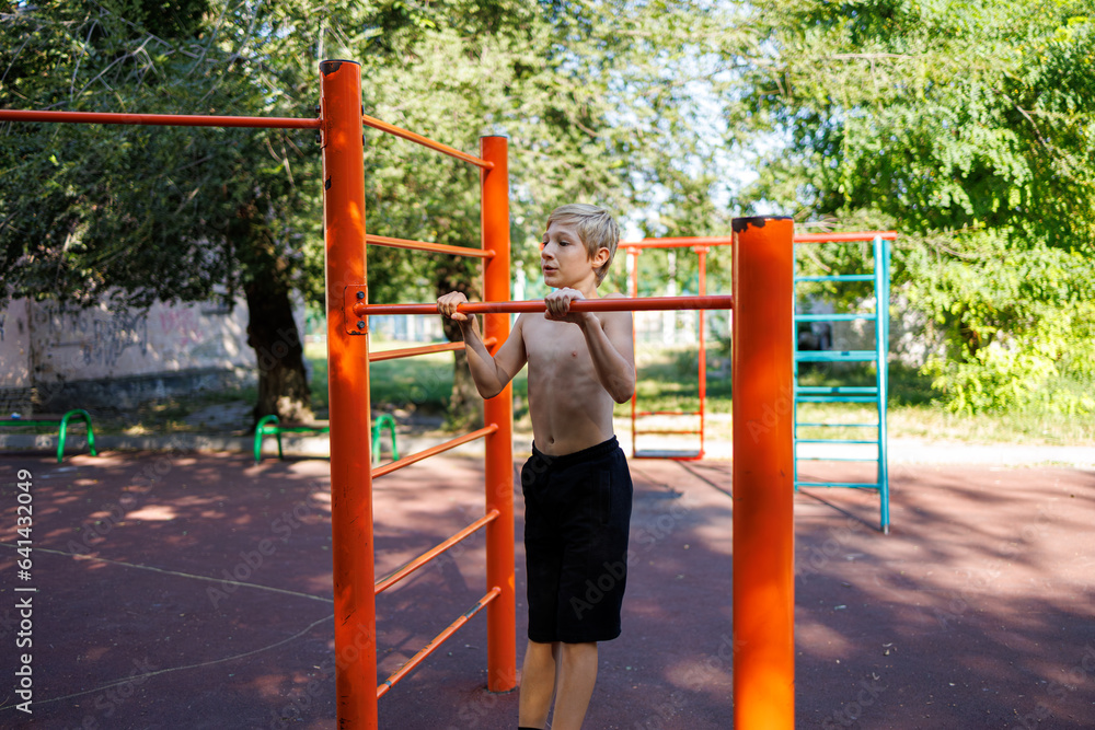 Fototapeta premium Sports boy performs exercises on the horizontal bar. Street workout on a horizontal bar in the school park.