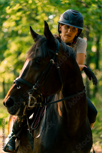 A rider dressed in a helmet rides her beautiful black horse in the forest during a horseback ride