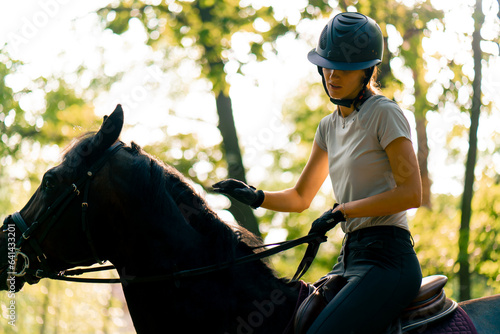 A rider dressed in a helmet rides her beautiful black horse in the forest during a horseback ride
