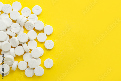 Heap of white pills on yellow background