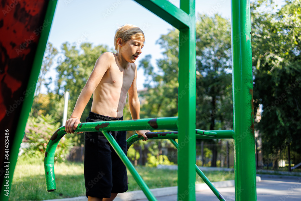 Fototapeta premium A sports child performs push-ups on sports bars. Street workout on a horizontal bar in the school park.