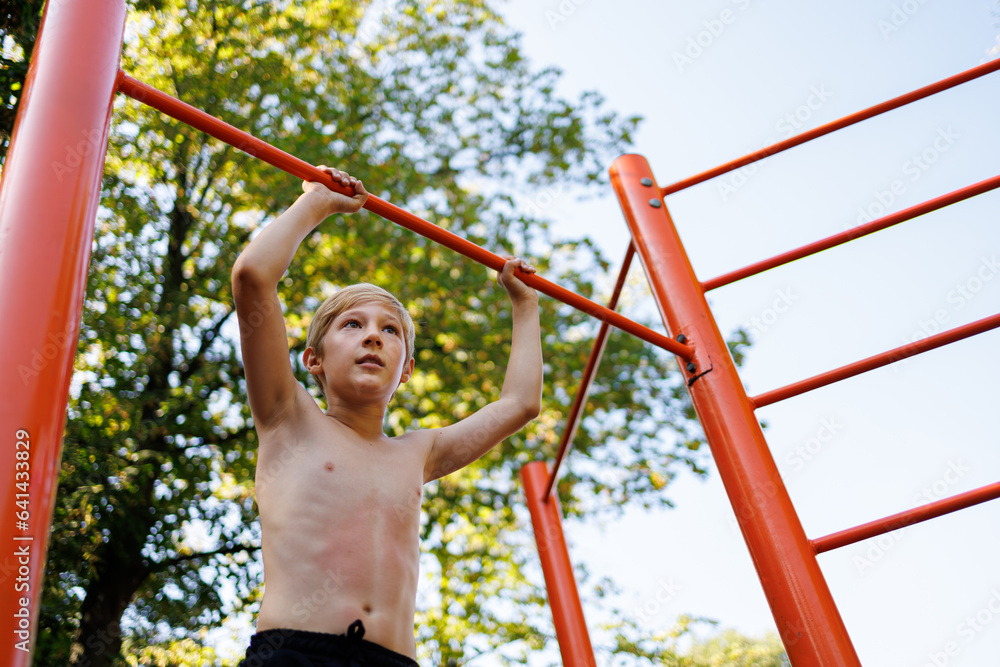 Fototapeta premium Bottom view of a gymnast boy holding on to a sports bar. Street workout on a horizontal bar in the school park.