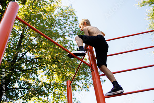 Bottom view of a teenager climbing on a gymnastics bar. Street workout on a horizontal bar in the school park.