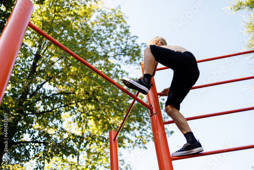 Bottom view of a teenager boy who climbs on a sports horizontal bar. Street workout on a horizontal bar in the school park.