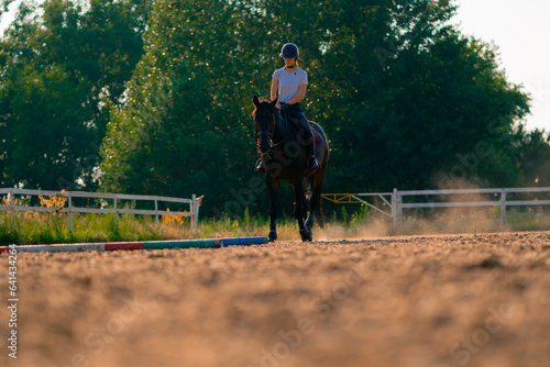 A rider dressed in a helmet rides her beautiful black horse in a riding arena during a horseback ride