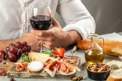 Hands holding a glass of wine and a wooden board with different kinds of cheese and ham, prosciutto, jamon salami, Antipasto Dinner or aperitivo party concept photo