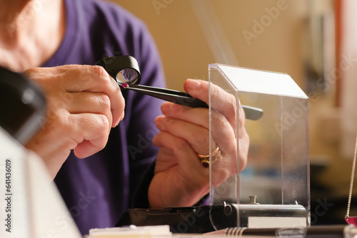 A gem specialist analizing a red ruby gemstone using tweezers and a loupe lense. Close up image of a gemologist evaluating a gemstone. concept of Gemstone identification. photo