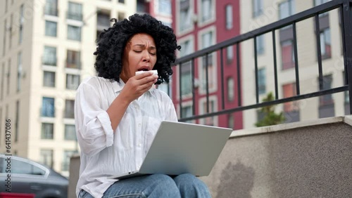 African American Lady Sneeze, Tissue and Runny Nose While Working on Laptop Sitting Outside. Business Girl Having Allergies and Feeling Unwell. Woman Sneezing and Suffering Flu, Cold, and Allergy photo