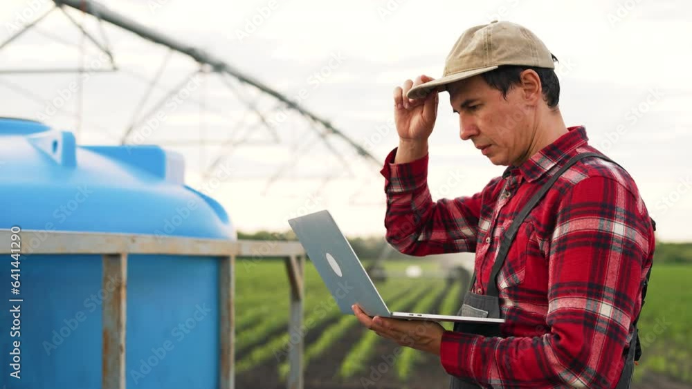 Agriculture.Farmer engineer is work with laptop in field.Automatic irrigation system for organic products on farm.Work engineer adjusts operation of irrigation system on farm.Agriculture food concept Agriculture.Farmer engineer is work with laptop in field.Automatic irrigation system for organic products on farm.Work engineer adjusts operation of irrigation system on farm.Agriculture food concept