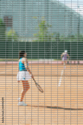 Girl girl playing tennis on court, sunny day. Blurred sport background