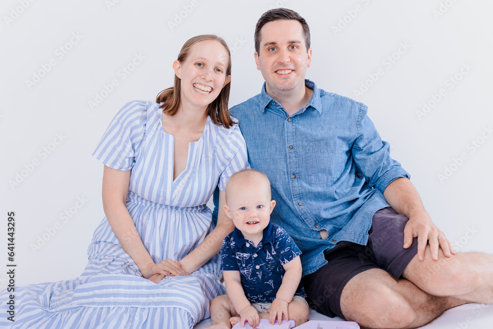 One year old baby boy on bed with parents sitting behind him smiling