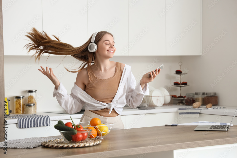 Happy young woman listening to music and dancing in modern kitchen