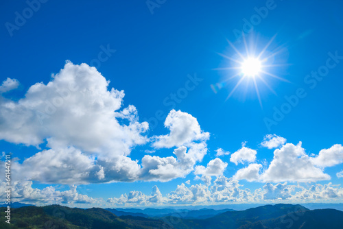 bright sun shines on the blue sky with with clouds over the mountain.