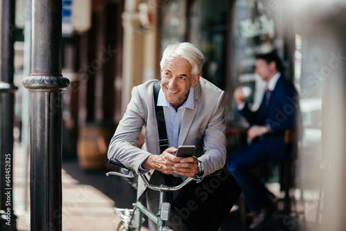 Mature businessman using a smart phone while commuting to work with his bicycle photo