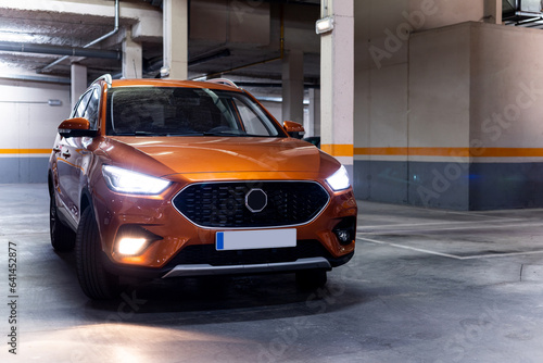 Front view of a modern orange SUV with its lights on is parked inside an underground car park. Car advertising concept.Modern orange SUVs. ©  Yistocking