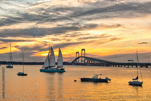 Sailboats at rest in Newport Rhode Island harbor as a peaceful sun sets behind the Newport bridge