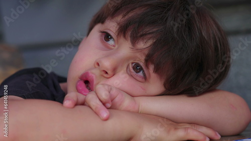 Close-up of bored child drooling and gazing in the distance, daydreamin and lost in thought, close-up face of kid in deep boredom