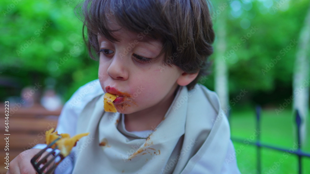 Messy small boy eating pasta for lunch in outdoors sunny setting. Portrait close-up face of child savoring noodles Messy small boy eating pasta for lunch in outdoors sunny setting. Portrait close-up face of child savoring noodles