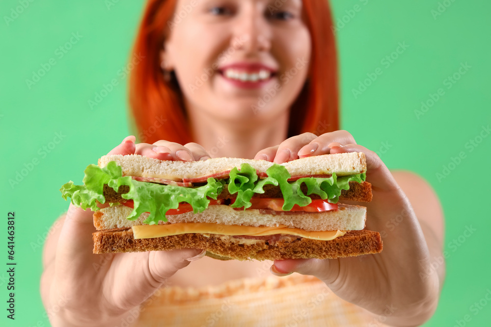 Young woman with tasty sandwich on green background, closeup