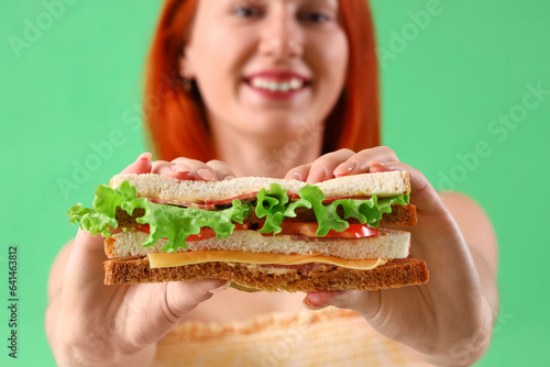 Young woman with tasty sandwich on green background  closeup