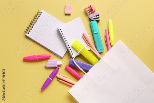 Composition with paper bag and different stationery on yellow background