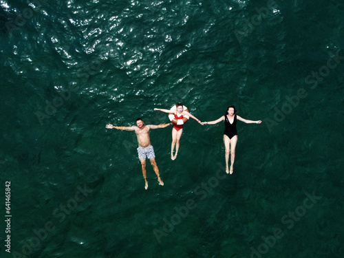 Happy summer holidays with family. Father, mother and little daughter on floating circle in swimsuits are lying and relaxing on sea water surface. Mom, dad and child spending time together at vacation