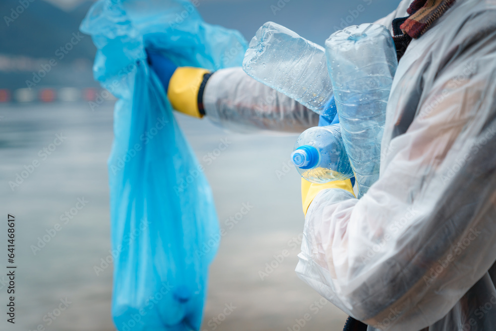 Fototapeta premium Photo of unknown person while holding garbage bag and plastic bottles in arms.