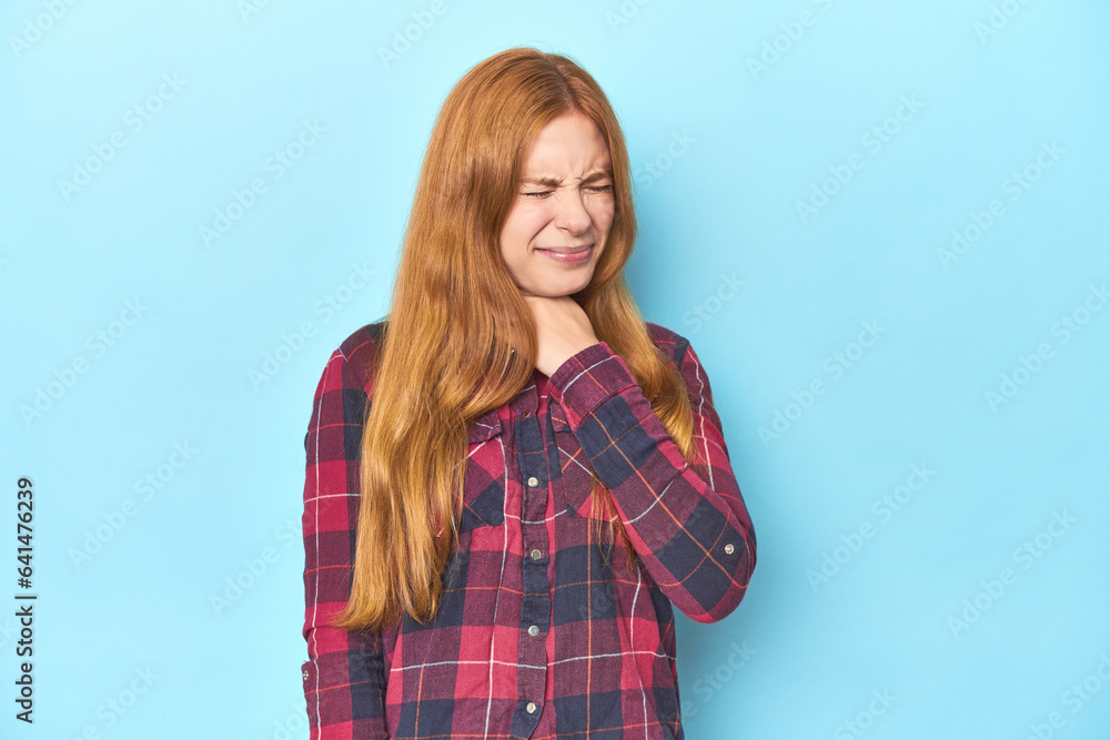 Redhead young woman on blue background suffers pain in throat due a virus or infection. Redhead young woman on blue background suffers pain in throat due a virus or infection.