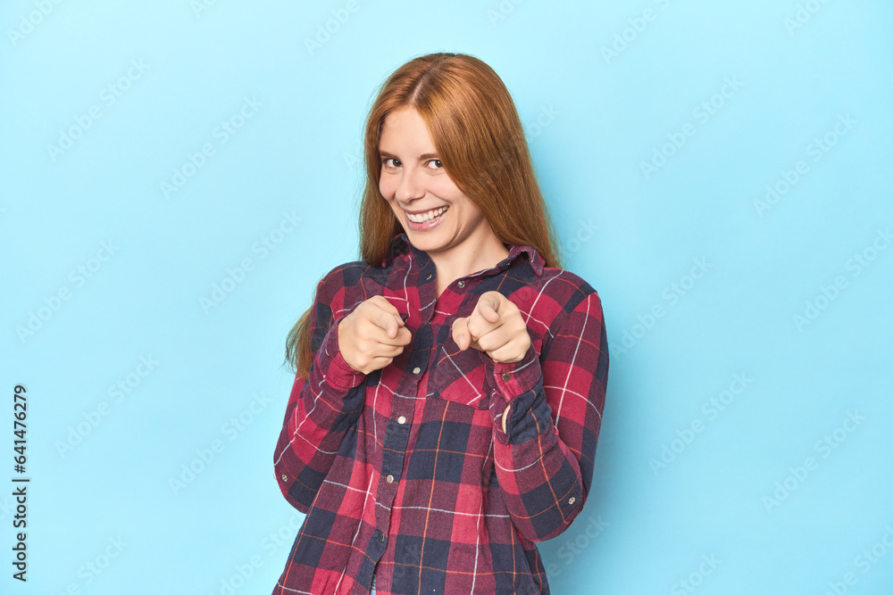 Redhead young woman on blue background pointing to front with fingers. Redhead young woman on blue background pointing to front with fingers.