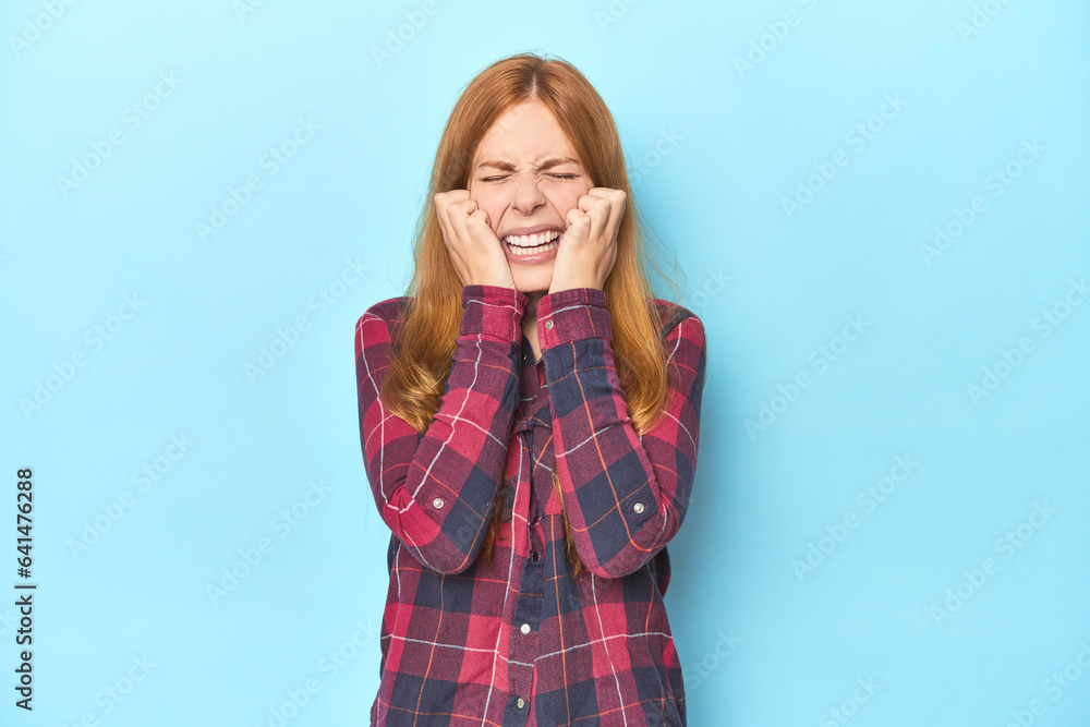 Redhead young woman on blue background crying, unhappy with something, agony and confusion concept. Redhead young woman on blue background crying, unhappy with something, agony and confusion concept.