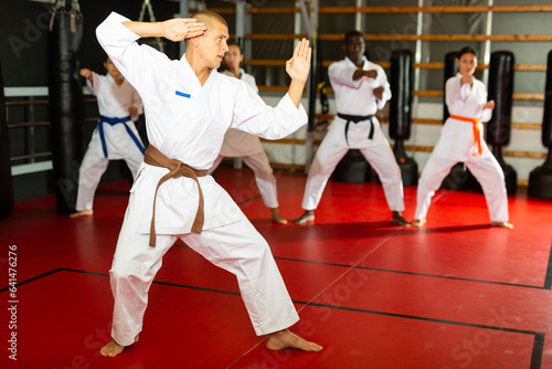 Caucasian man in kimono standing in fight stance during group karate training.