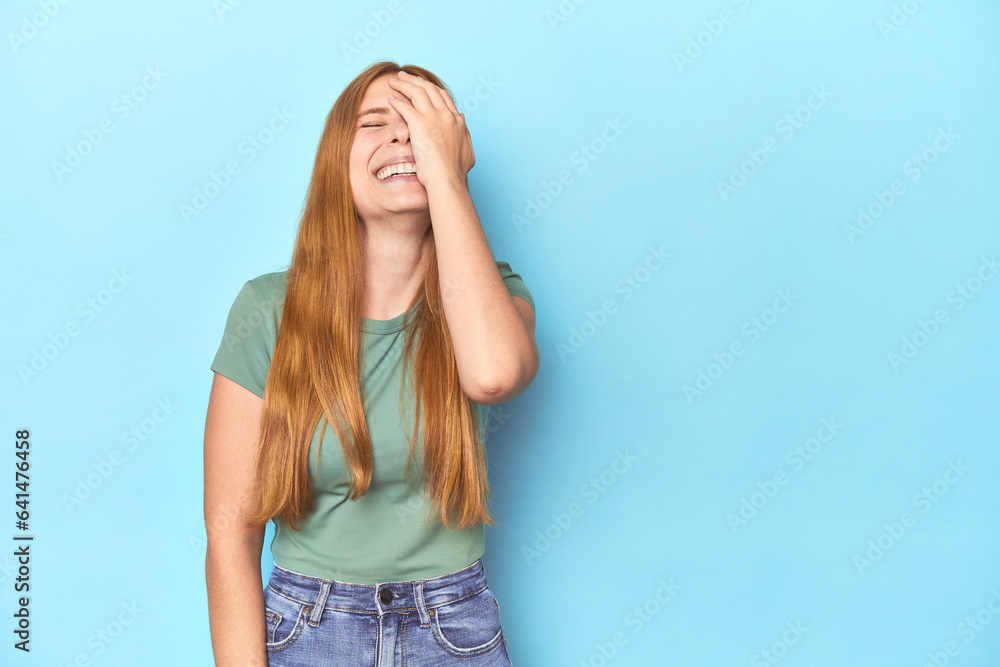 Redhead young woman on blue background laughing happy, carefree, natural emotion. Redhead young woman on blue background laughing happy, carefree, natural emotion.