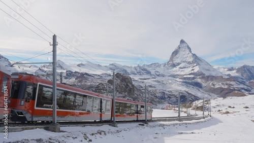 4K Static Shot of Gornergrat bahn railway climibing up the summit station with Matterhorn mountain peak background in Zermatt on a sunny winter day. Swiss Alps, Switzerland travel journey trip.