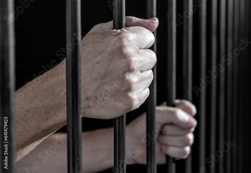 Fotografie Prisoner's hands gripping the bars of a cell in jail or prison serving sentence