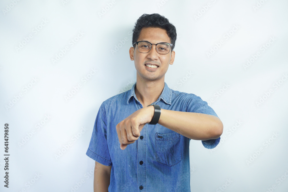 Portrait of an Asian man wearing a blue shirt smiling looking at his watch on a white background Portrait of an Asian man wearing a blue shirt smiling looking at his watch on a white background