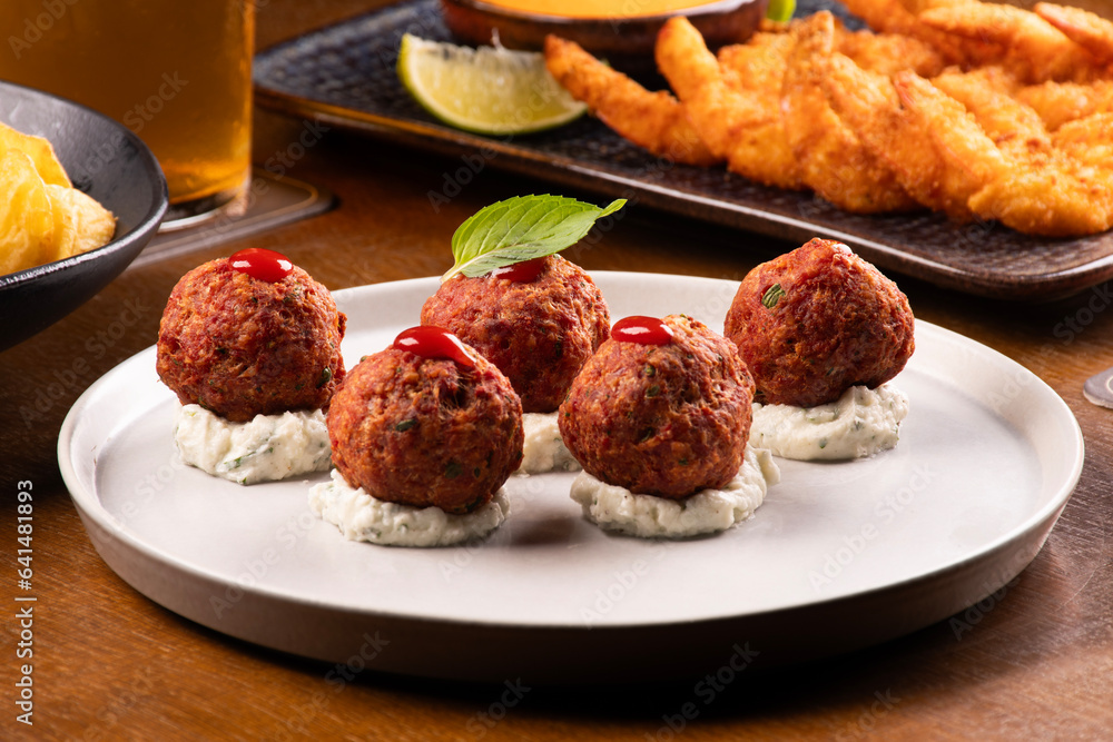 closeup on chili meatballs appetizers and plate of breaded prawns blurred in the background happy hour at the beer pub closeup on chili meatballs appetizers and plate of breaded prawns blurred in the background happy hour at the beer pub