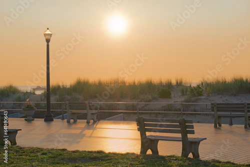 sunrise or sunset with boardwalk beach dunes park benches and a lamppost in summer photo