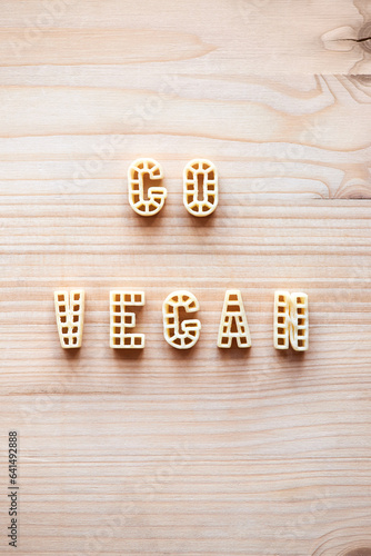 Inscription ‘Go vegan’ written with alphabet pasta on wooden table, directly above view  photo