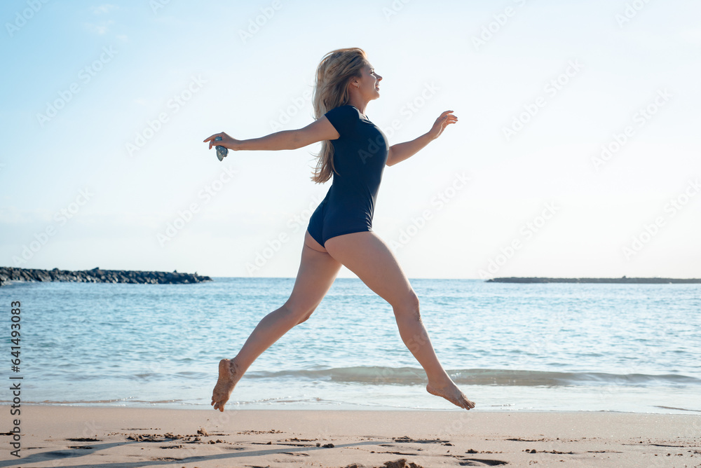 A young successful gymnast in a black swimsuit shows her skills on the beach by the sea in Georgia A young successful gymnast in a black swimsuit shows her skills on the beach by the sea in Georgia